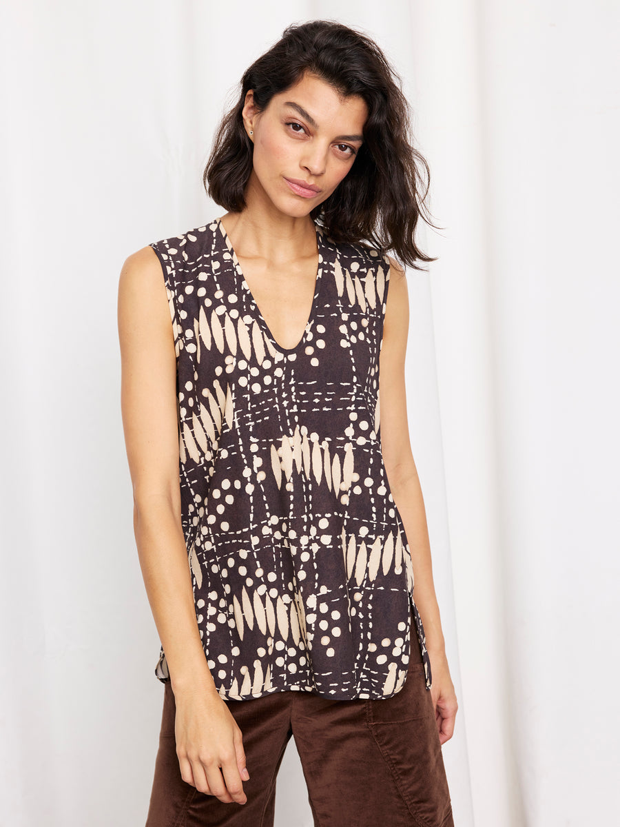 A woman with shoulder-length dark hair models the Zero + Maria Cornejo Ony Tank—a sleeveless silk top featuring a black and beige abstract print—paired with brown pants, set against a white background.