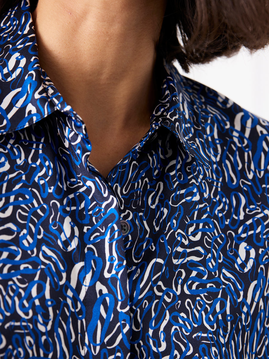 Close-up of a person wearing the Circle Shirt by Zero + Maria Cornejo, featuring an abstract blue, white, and black squiggly pattern. Only the neck, chin, and part of shoulder-length dark hair are visible.