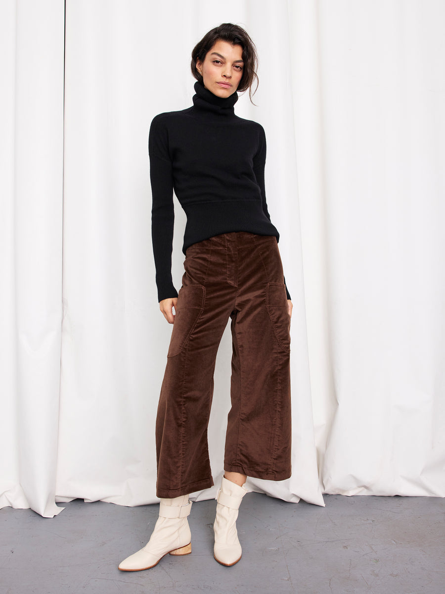 Indoors, a person wears a black turtleneck sweater, white ankle boots, and the Curved Eda Culotte by Zero + Maria Cornejo. White curtains are in the background. The look offers modern style and comfort, crafted in New York.