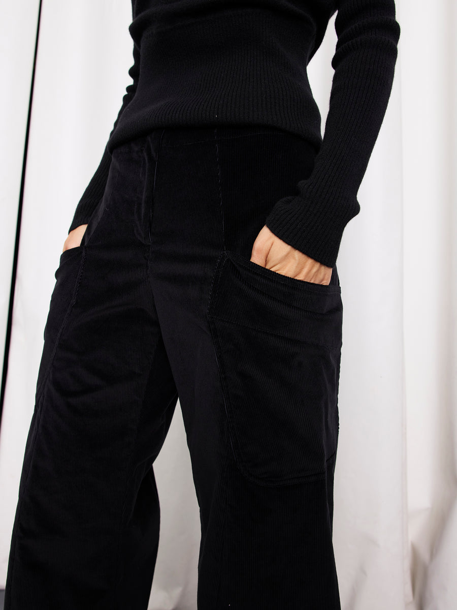 A person wearing a black ribbed sweater and Zero + Maria Cornejo’s Curved Eda Culotte stands with hands in their pockets against a white background.