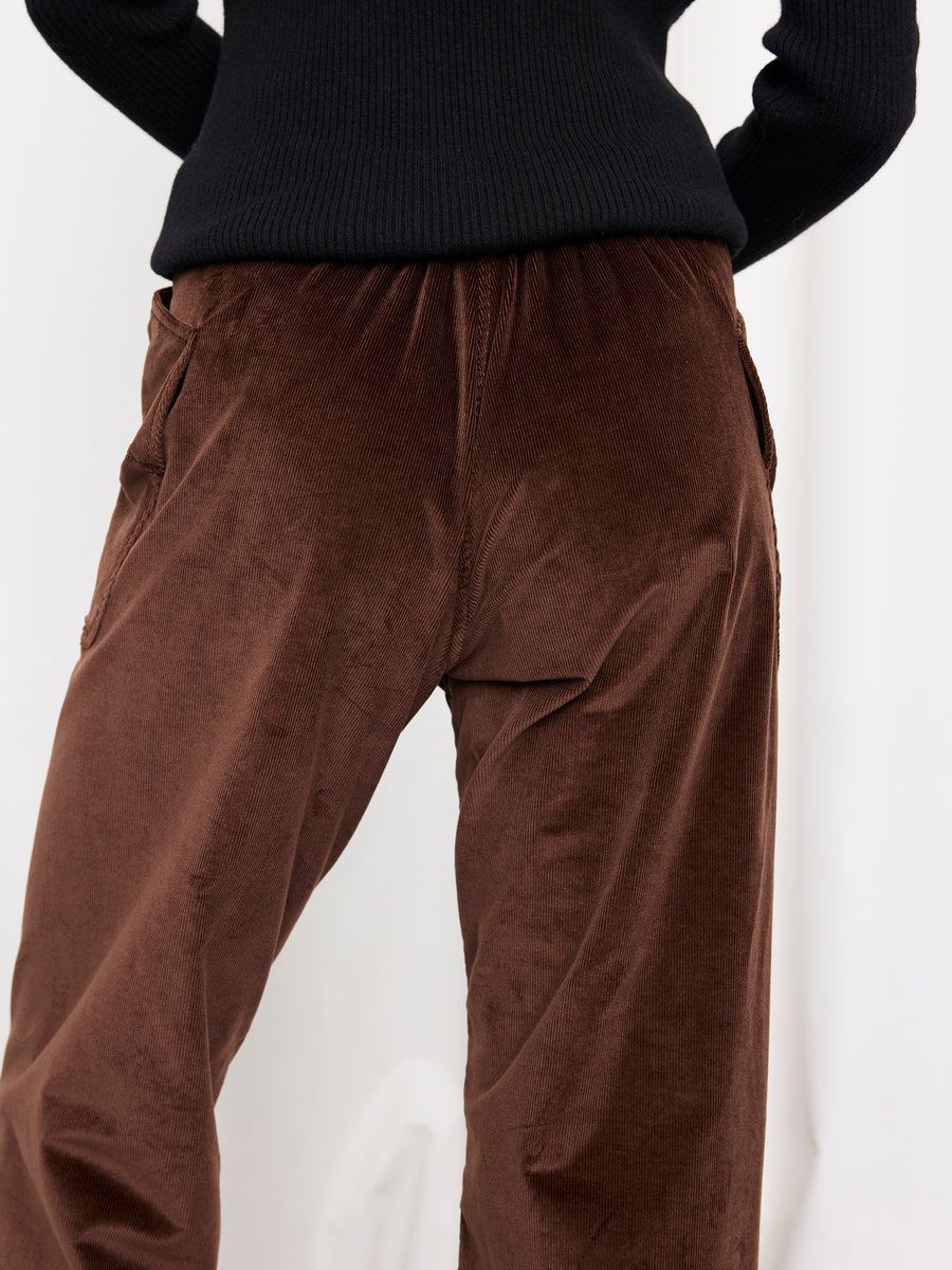 A person is shown from mid-torso to thighs against a plain light background, wearing the Eda Pant by Zero + Maria Cornejo—brown wide leg corduroy pants paired with a black ribbed sweater.