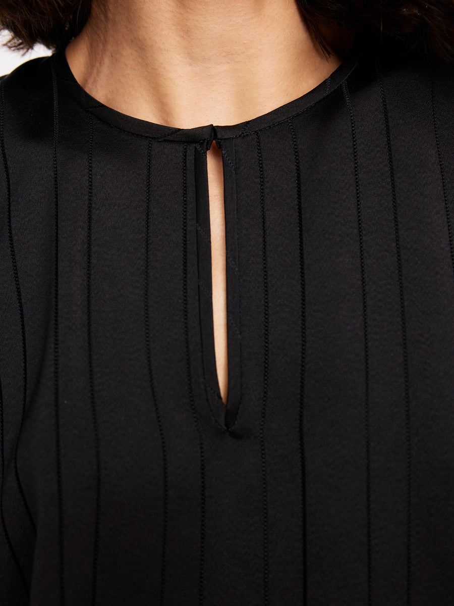 Close-up of a person wearing the Rae Poncho Top by Zero + Maria Cornejo, featuring woven stripes, vertical stitched lines, and a small neckline slit; this elegant sheen blouse is made in New York.