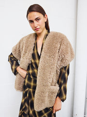 A person in a plaid dress and the Reversible Saban Waistcoat by Zero + Maria Cornejo stands against a white wall, looking at the camera with one hand on their hip.