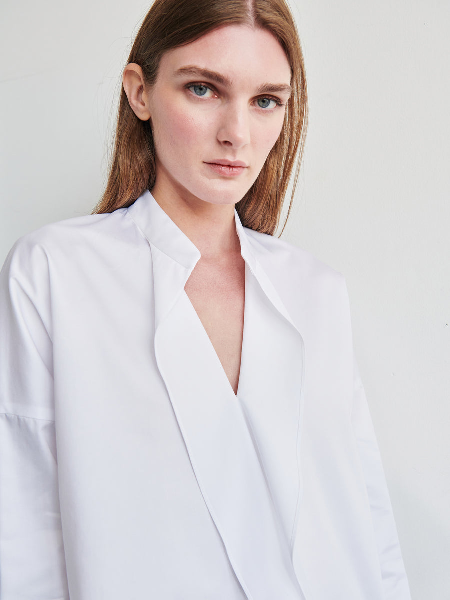 A person with long, straight hair and a serious expression is wearing the Long-Sleeved Fin Gaban Shirt by Zero + Maria Cornejo. They are standing against a plain white background, gazing directly at the camera.