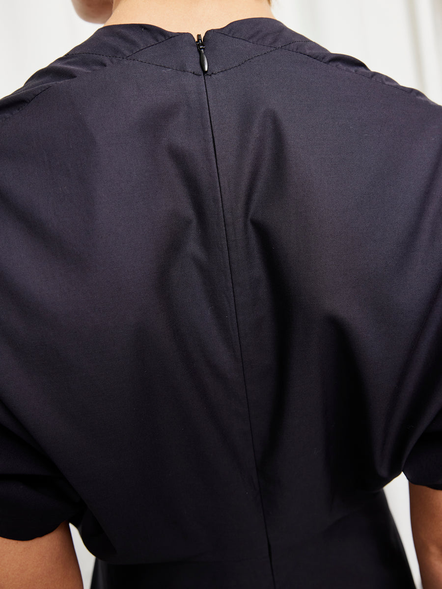 Close-up of the back of a person wearing the Long Aki Wave Dress by Zero + Maria Cornejo. The dark cotton broadcloth features smooth fabric, soft folds, and stitching details, with a visible neckline zipper. Made in New York.
