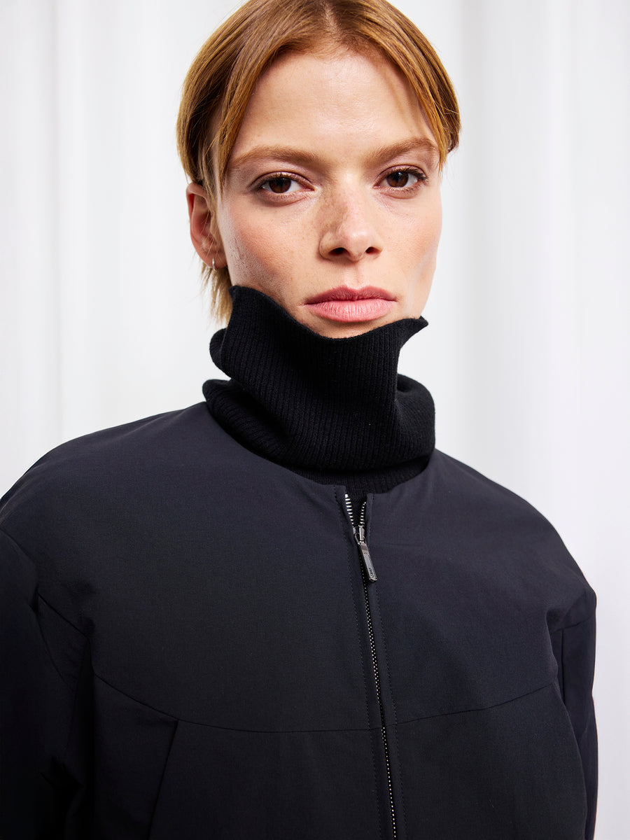 A person with short, light brown hair wears the Zero + Maria Cornejo T Bomber over a black turtleneck, standing against a white background and looking directly at the camera with a neutral expression.