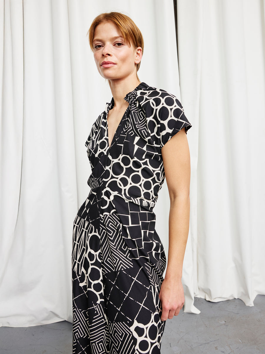 A person with short hair stands in front of white curtains, wearing the Long Ruched Stella Dress by Zero + Maria Cornejo.