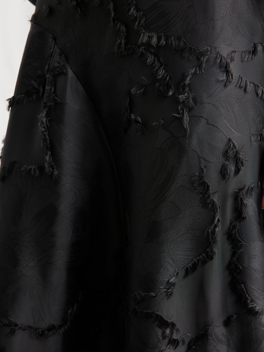 Close-up of black FSC viscose fabric with a textured floral pattern and frayed details, featured on the Circle Skirt by Zero + Maria Cornejo, blending smooth and rough surfaces for a sustainable, elegant finish.