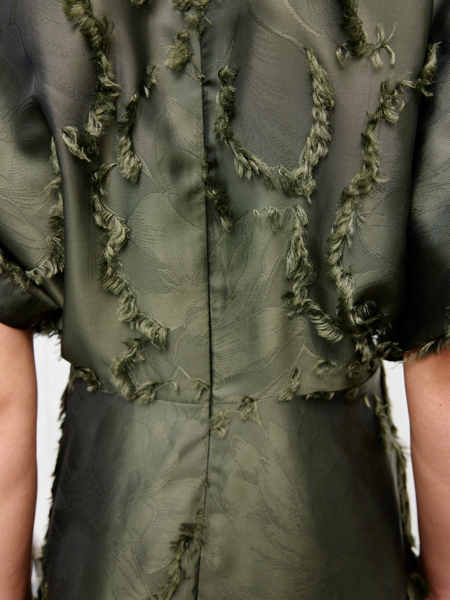 Close-up of the back of the green Long Aki Wave Dress by Zero + Maria Cornejo, featuring fil coupé jacquard with frayed, raised leafy patterns, short sleeves, and a visible vertical center seam.