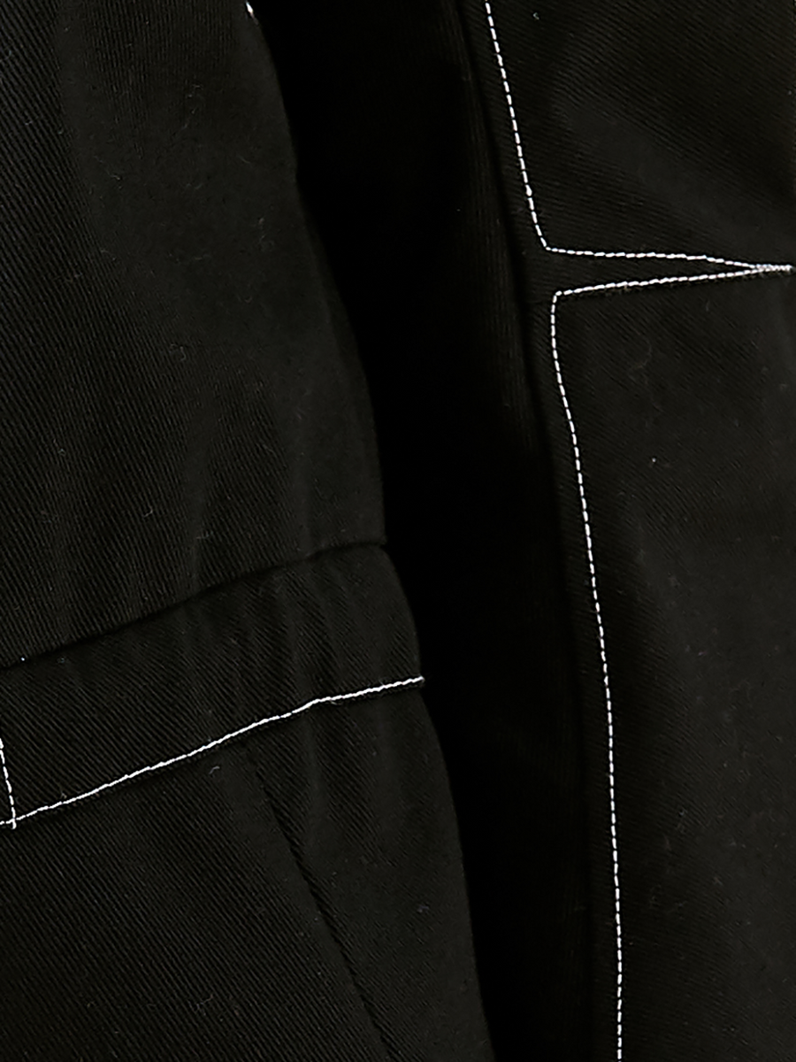 Close-up of black fabric with white stitching on the Ari Waistcoat by Zero + Maria Cornejo. The stitching forms angular patterns, contrasting against the dark material and creating a geometric design. Made from GOTS-certified cotton, it embodies both style and sustainability.