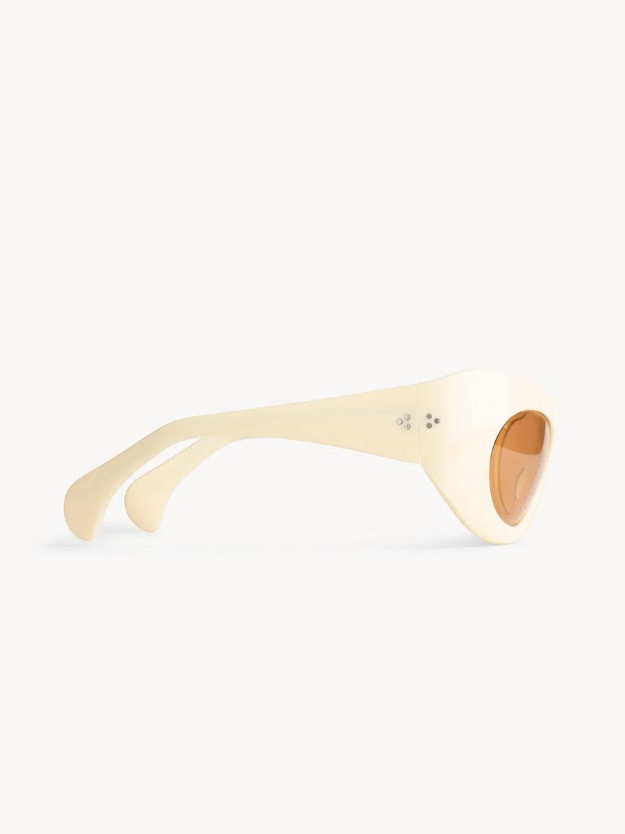 Side view of Port Tanger Ruh cream-colored, thick-framed sunglasses by Port Tanger, featuring brown-tinted oval lenses with 100% UVA/UVB protection, set against a plain white background.