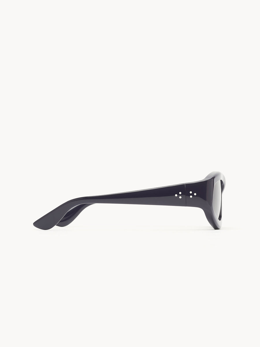 Side view of Port Tanger Irfan sunglasses by Port Tanger, featuring thick, glossy black frames with visible hinges and UVA/UVB protection, displayed on a plain white background.