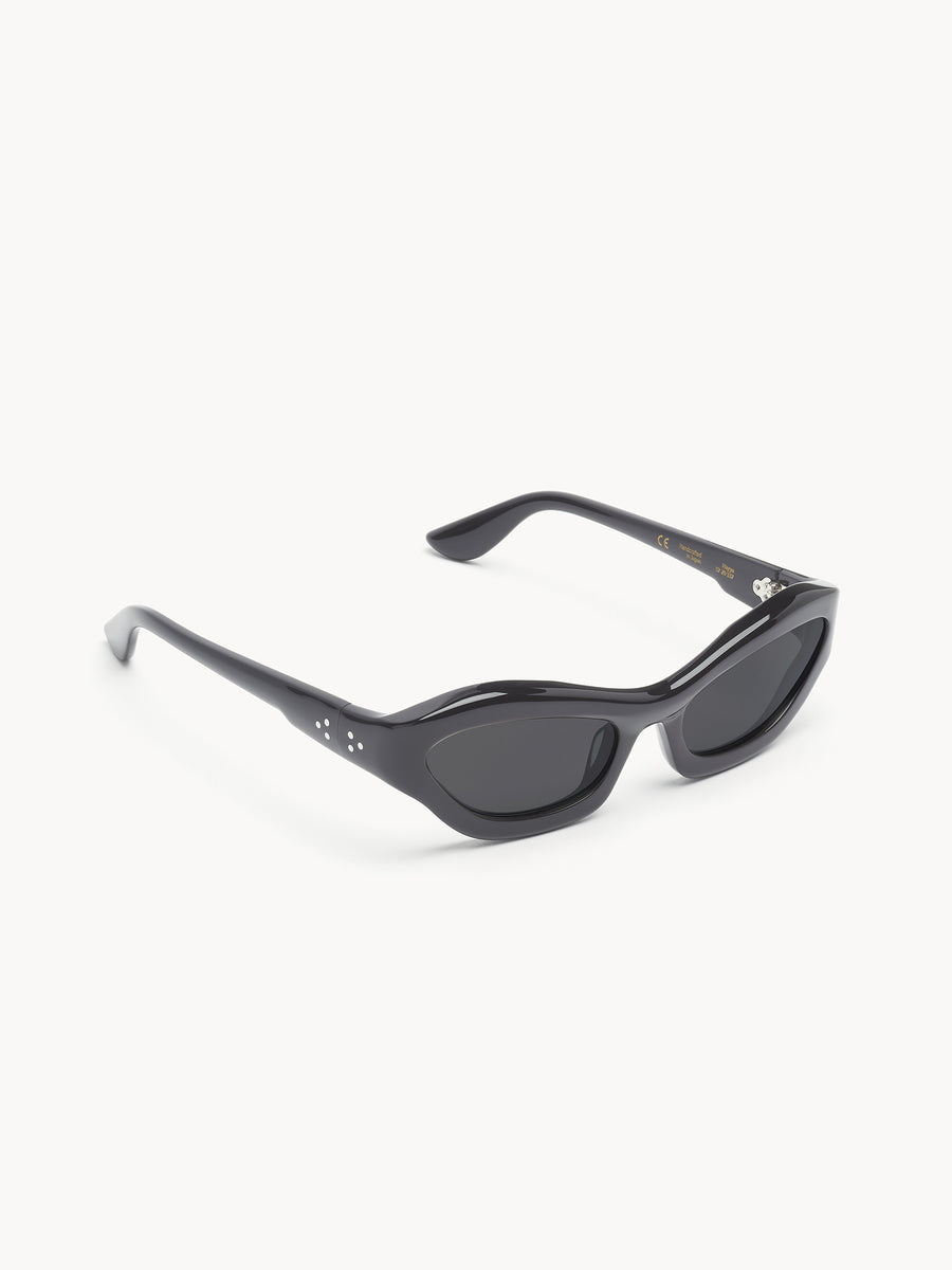 The Port Tanger Hayya by Port Tanger are black cat-eye sunglasses with dark lenses and thick, glossy frames that offer UVA/UVB protection. These unisex sunglasses combine style and safety on a white background.