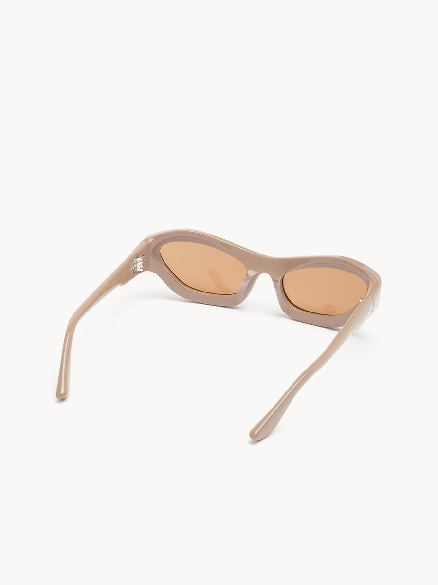 The Port Tanger Hayya by Port Tanger features beige cat-eye frames and rounded amber lenses. Shown from the back and at an angle on a white background, these unisex sunglasses offer style with essential UVA/UVB protection.
