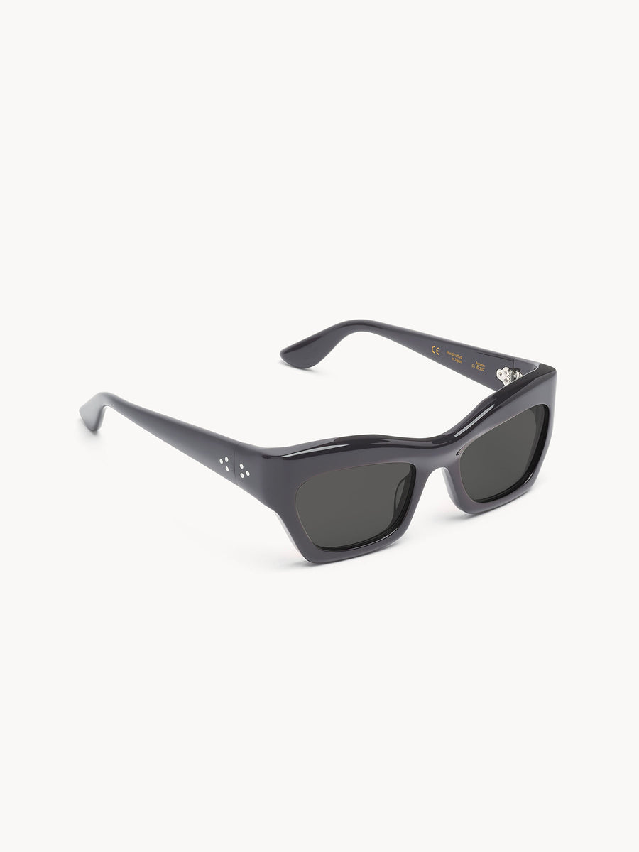 Port Tanger Ayreen by Port Tanger: black rectangular sunglasses with thick, glossy frames and dark lenses, handmade in Japan. They feature a subtle three-dot detail near the hinges and provide 100% UVA/UVB protection.