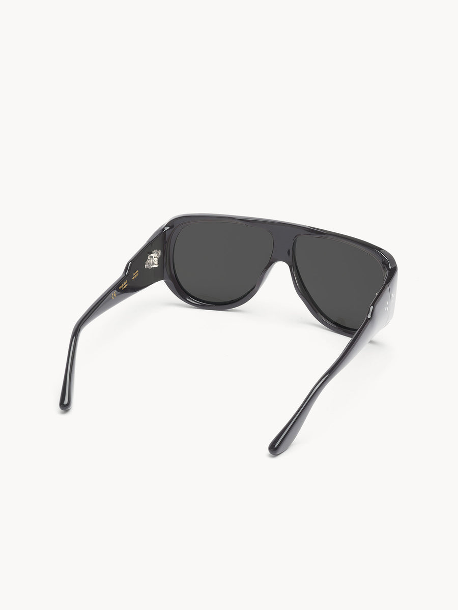 The Port Tanger Gambia sunglasses by Port Tanger feature thick black frames and dark tinted lenses, displayed from the rear with slightly open arms on a white background. They provide reliable UVA/UVB protection.
