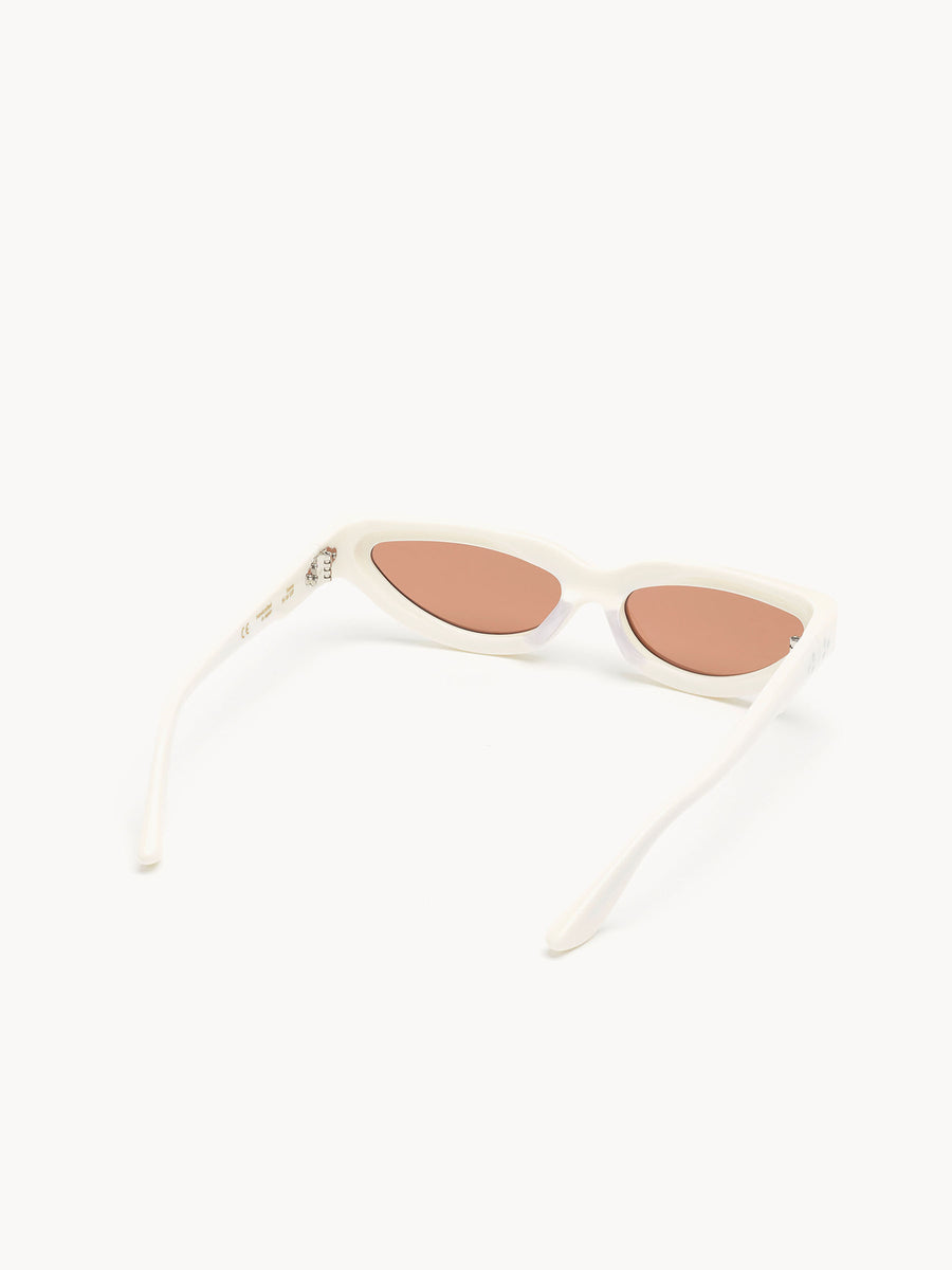 The Port Tanger Fanna cat-eye sunglasses by Port Tanger feature white frames and pink-tinted lenses, handcrafted in Japan with 100% UVA/UVB protection, seen resting on a white surface and photographed from behind.