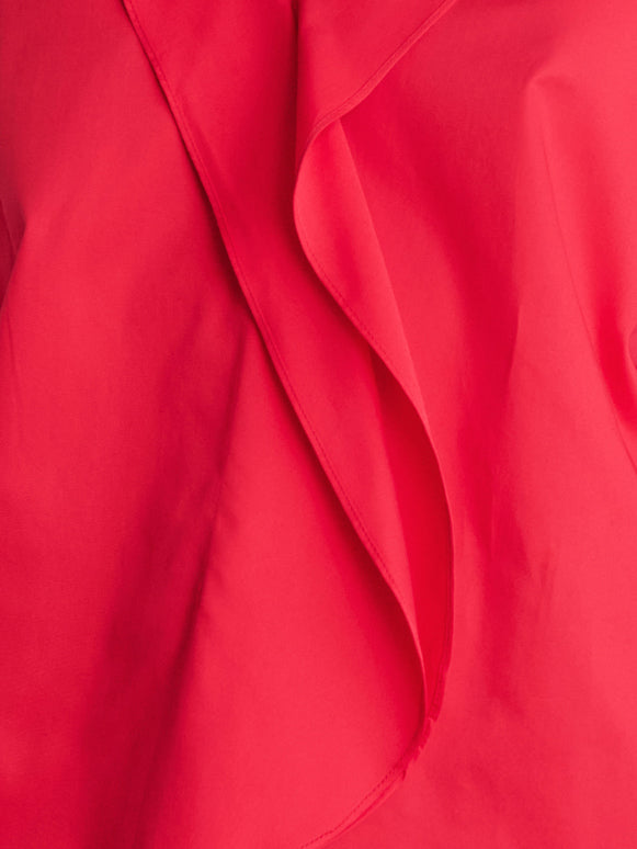 A close-up of the Fin Gaban Dress by Zero + Maria Cornejo features a vibrant red fabric with a prominent fold creating a draped collar effect. The material has a smooth texture, accentuating its fluidity and rich color, reminiscent of elegant cotton shirting.