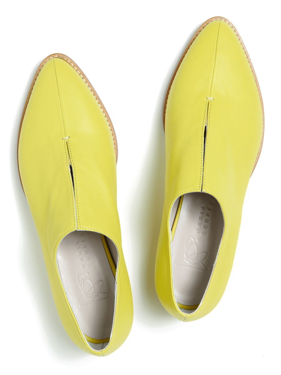 The Kiara Oxford by Zero + Maria Cornejo is a vibrant yellow pair of slip-on shoes made from luxurious Nappa leather. They feature pointed toes, subtle stitching, and natural brown soles with a wooden heel. Pictured from above on a white background, they're available in Italian sizing. Final sale item.