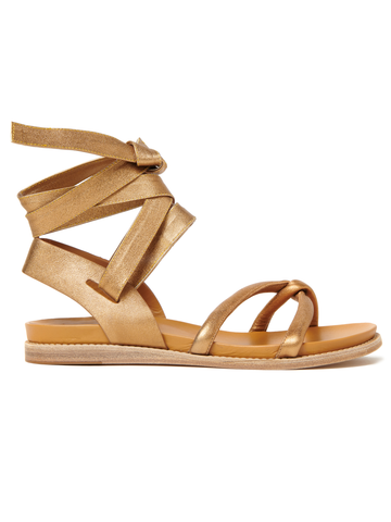 A single gold strappy metallic leather Limi Sandal by Zero + Maria Cornejo with a flat sole and an intricate design of crisscrossing straps that wrap around the ankle. The sandal has a simple yet elegant look, ideal for both casual and formal wear.