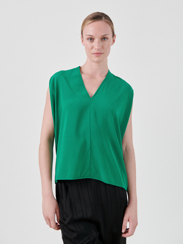 A person with blonde hair is wearing a sleeveless, green Ina Tank by Zero + Maria Cornejo and black pants. They are standing against a plain white background, looking directly at the camera with a neutral expression.