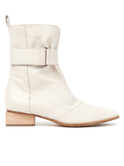 The Adina Boot by Zero + Maria Cornejo showcases a sleek, modern design with its side view in cream-colored Nappa leather. This ankle boot features a rounded toe and a mid-height wooden block heel, complemented by minimal stitching details. A wide strap with an adjustable Velcro closure wraps stylishly around the ankle.