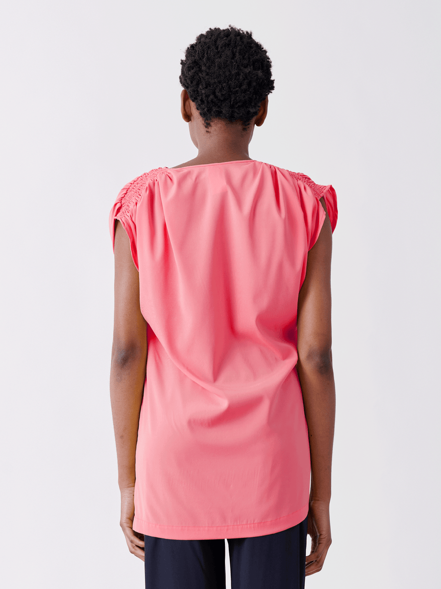 The individual wears the Ruched Fold Top by Zero + Maria Cornejo, a pink sleeveless silk charmeuse, with gathered shoulders, seen from behind against a plain white backdrop.