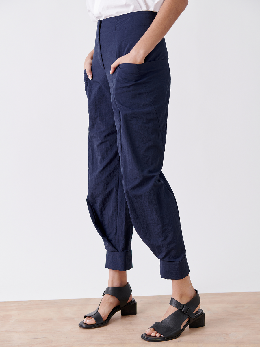 Against a light background, a person wears loose-fitting navy Akeo Jodhpur pants from Zero + Maria Cornejo with hands in the pockets and black heeled sandals visible.