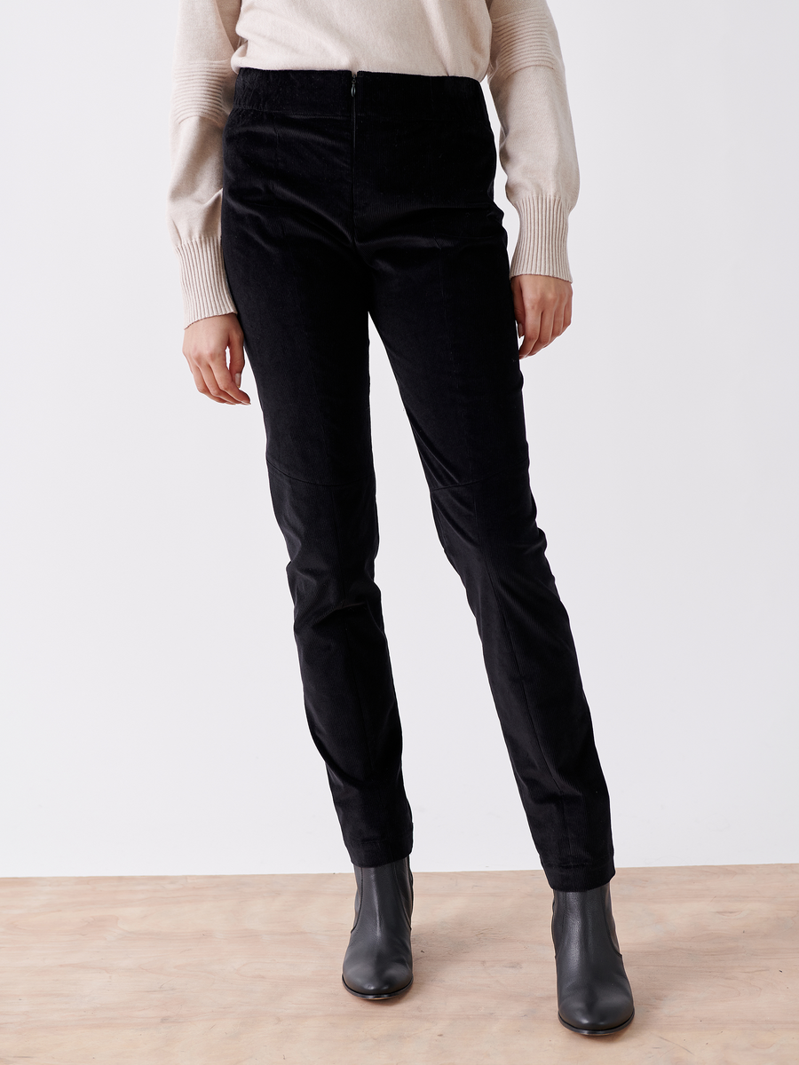 A person is standing on a wooden floor wearing the Slim Tala Trouser - Final Sale in black by Zero + Maria Cornejo with a beige sweater and black ankle boots. The photo captures them from the neck down against a plain white background.