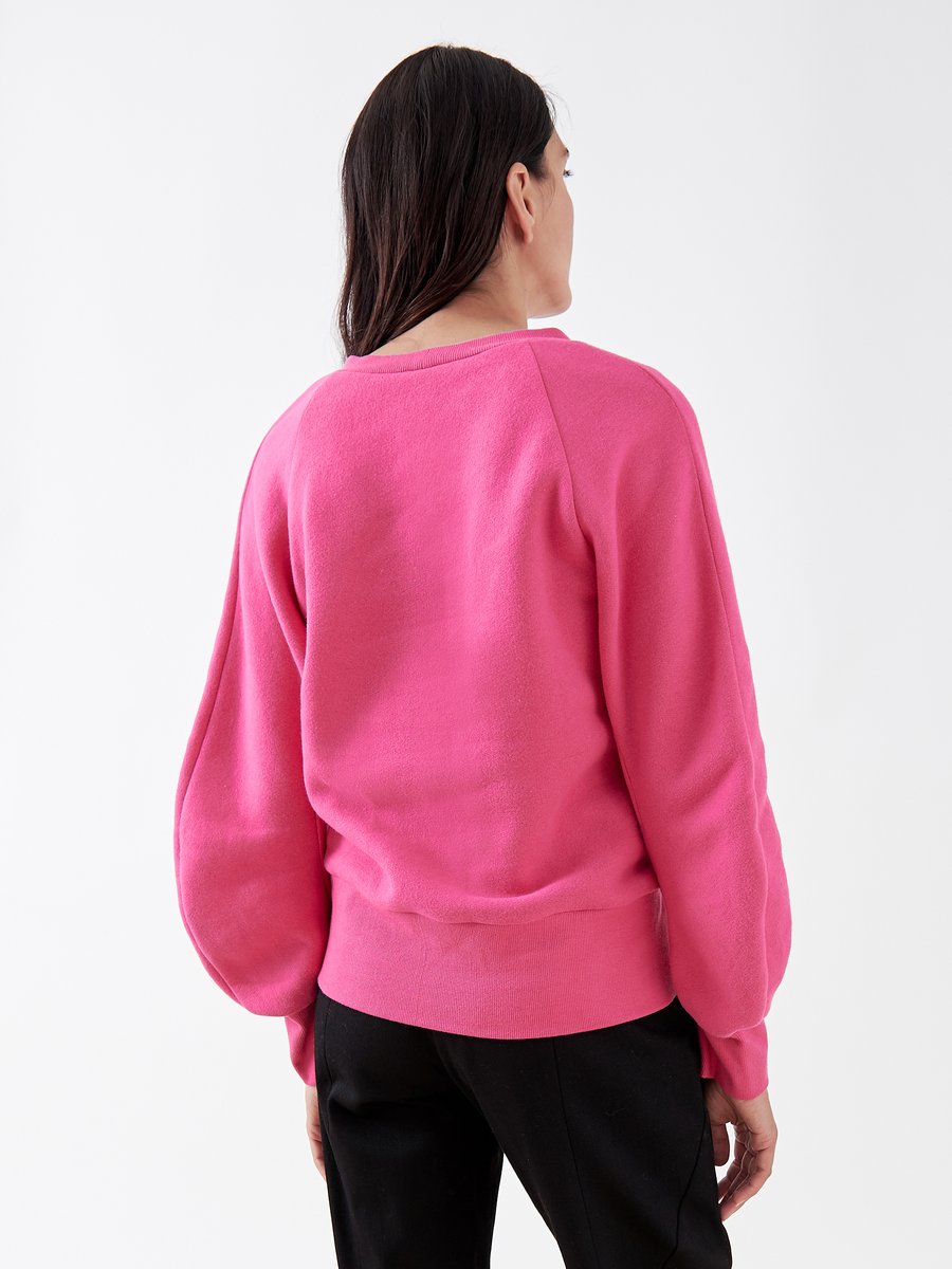 A person is wearing the B Sweatshirt - Final Sale by Zero + Maria Cornejo, a bright pink biodegradable fabric with voluminous sleeves, paired with black pants against a plain white background. Their back is to the camera.