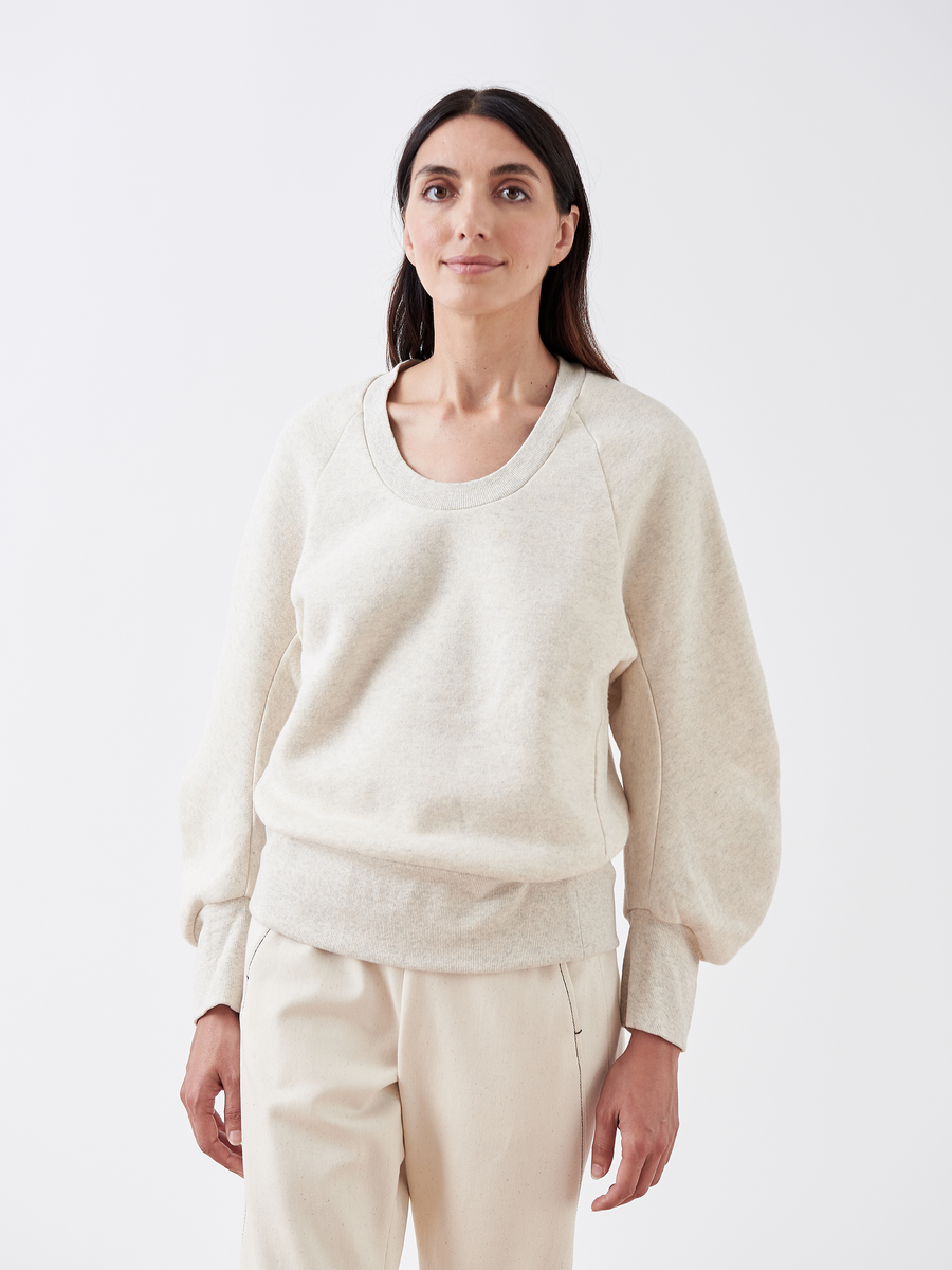 A person with long dark hair stands against a white backdrop, wearing the B Sweatshirt by Zero + Maria Cornejo, featuring puffed sleeves and matching pants made from biodegradable fabric, looking slightly to the side.