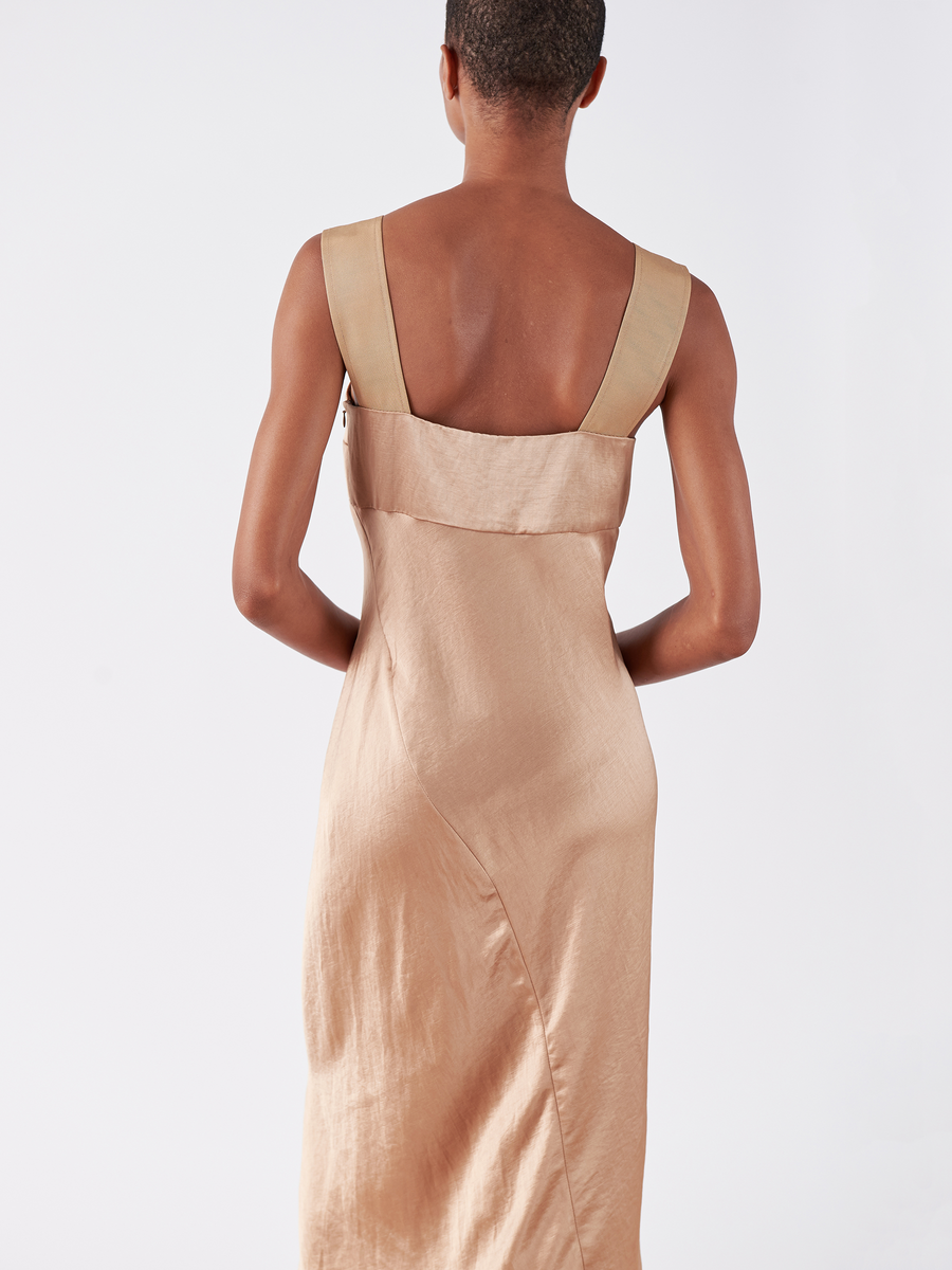 Rear view of a person in the stylish Bias Oona Dress by Zero + Maria Cornejo, featuring a square neckline, wide straps, fitted upper portion, and smooth beige satin with a subtle sheen. The plain white background enhances the dress's sophistication.