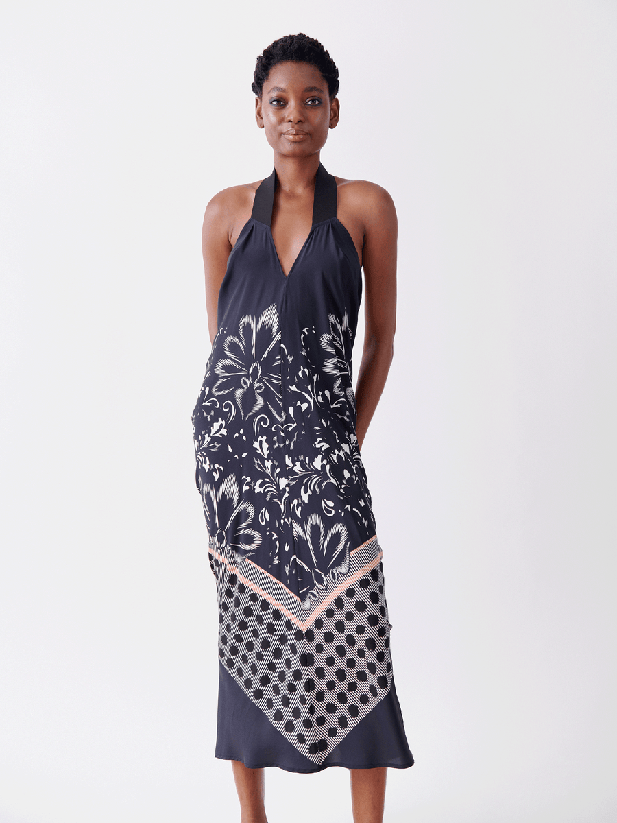 Wearing the Long Gigi Dress by Zero + Maria Cornejo, a person showcases elegance in a sleeveless, halter-neck silk dress adorned with floral and geometric patterns. The dress features bold floral prints and subtle polka dots near the hemline, highlighting its exquisite digital inkjet printing.