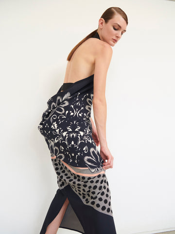 A woman with sleek brown hair poses against a plain white background, wearing the strapless, backless Long Gigi Dress by Zero + Maria Cornejo. The dress features intricate floral and polka dot patterns with a high slit and draped charmeuse fabric enhanced by digital inkjet printing.