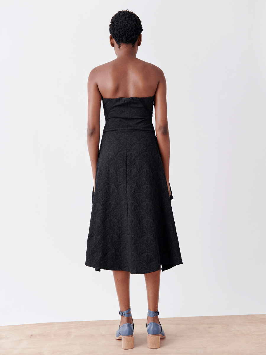 A person stands on a wooden surface, wearing the Strapless Nio Dress by Zero + Maria Cornejo and subtle-patterned blue platform sandals against a plain white background.