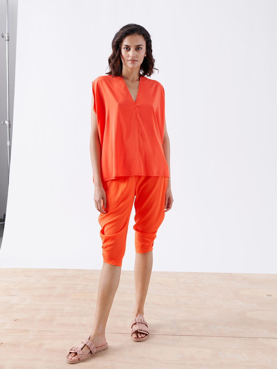 A person stands on a wooden floor wearing a vibrant orange outfit with a V-neck top and the 