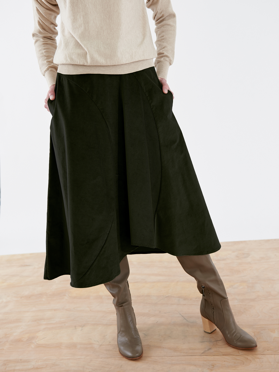 On a wooden floor, a person wears a beige sweater, brown heeled boots, and a Zero + Maria Cornejo Circle Swing Skirt - Final Sale, the photo cropped at the waist to emphasize the outfit.