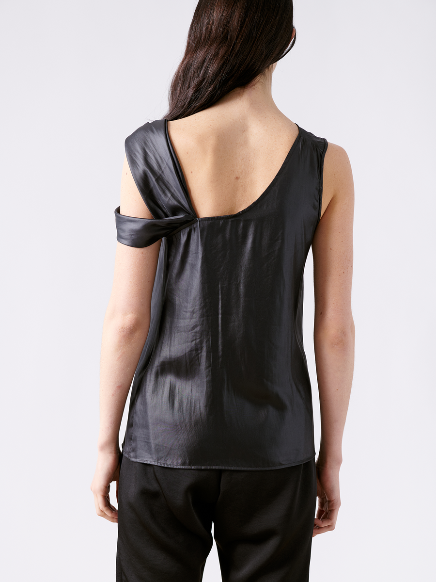 The image shows the back of someone wearing Zero + Maria Cornejo's chic black Ampe Top, paired with black pants. With asymmetric knot detail and elegantly twisted fabric around one arm, this sleeveless top is made from recycled polyester and stands out against a plain white background.