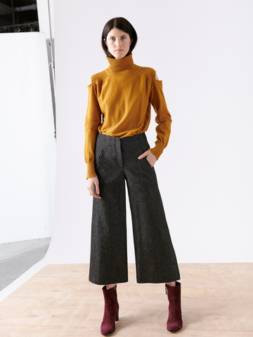 A person on a wooden floor with a white backdrop wears a mustard turtleneck, Zero + Maria Cornejo 