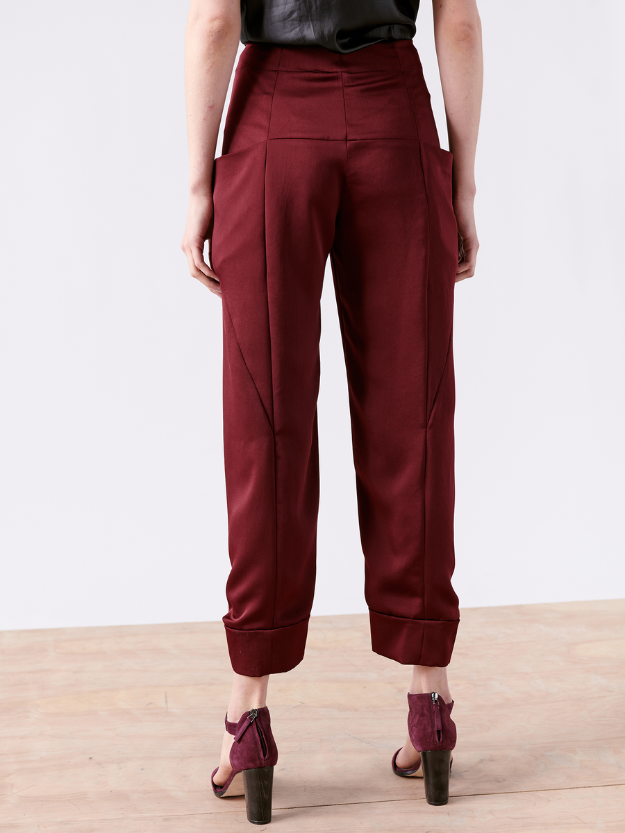 A person poses back-to-camera on a light wooden floor, wearing maroon Akeo Jodhpur pants by Zero + Maria Cornejo with large side pockets, made from 100% recycled fabric. Paired with a black top and maroon open-toe heels, they epitomize sustainable style made in New York.