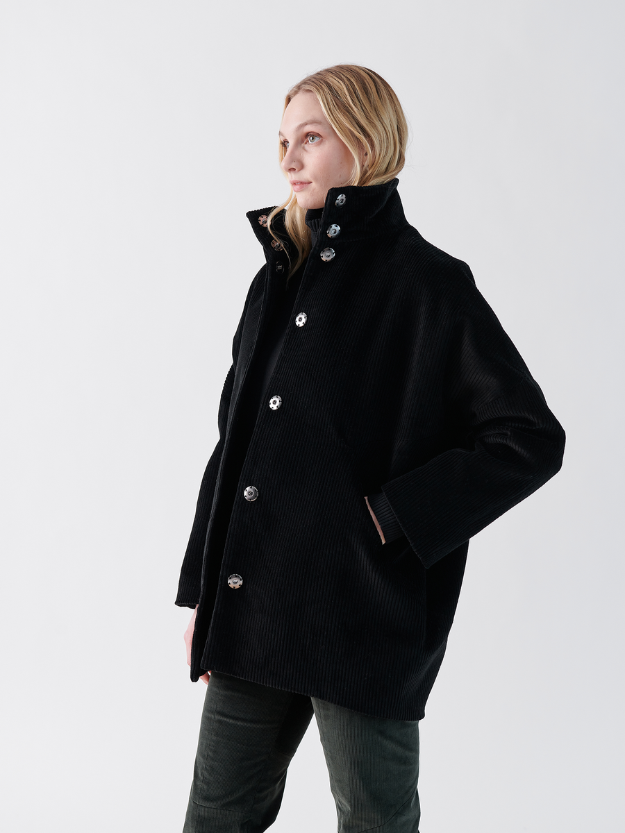 A person with long blonde hair wears a Long-Sleeved Bea Parka by Zero + Maria Cornejo and soft green cotton pants. They stand in front of a plain white background, looking to their right.