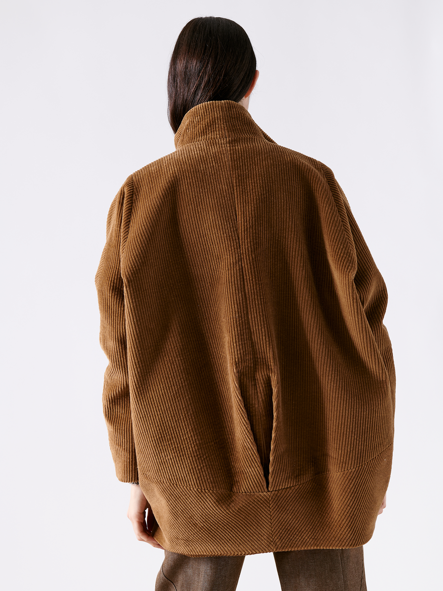 A person with long dark hair wears the oversized Long-Sleeved Bea Parka by Zero + Maria Cornejo. The back view shows its corduroy texture, relaxed fit, and subtle funnel collar against a plain white background.