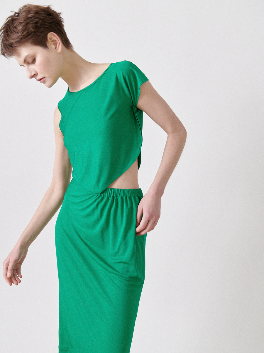 A person is wearing a vibrant green Cut Out Triangle Dress by Zero + Maria Cornejo, featuring an asymmetrical cut-out, while standing against a plain white background.