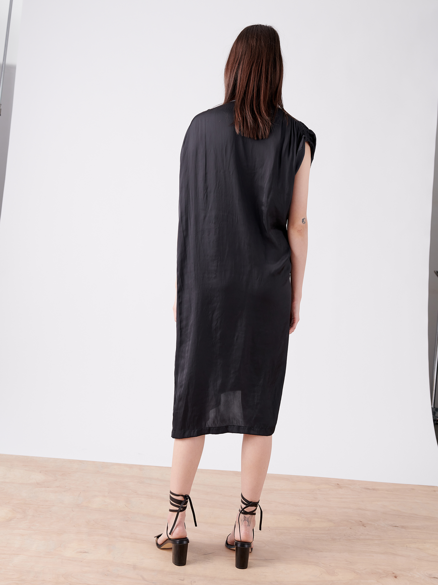 A person with long hair wears the Ruched Fold Dress by Zero + Maria Cornejo, standing on a wood floor against a white backdrop, highlighting black lace-up high-heeled sandals.