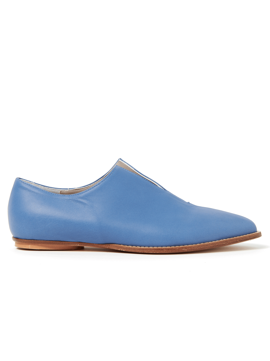 The Kiara Oxford from Zero + Maria Cornejo is a minimalist blue leather slip-on with a smooth surface, low profile, and light brown wooden heel against a plain white background. Crafted in Italian sizing for the perfect fit, it epitomizes effortless style. Final Sale item.