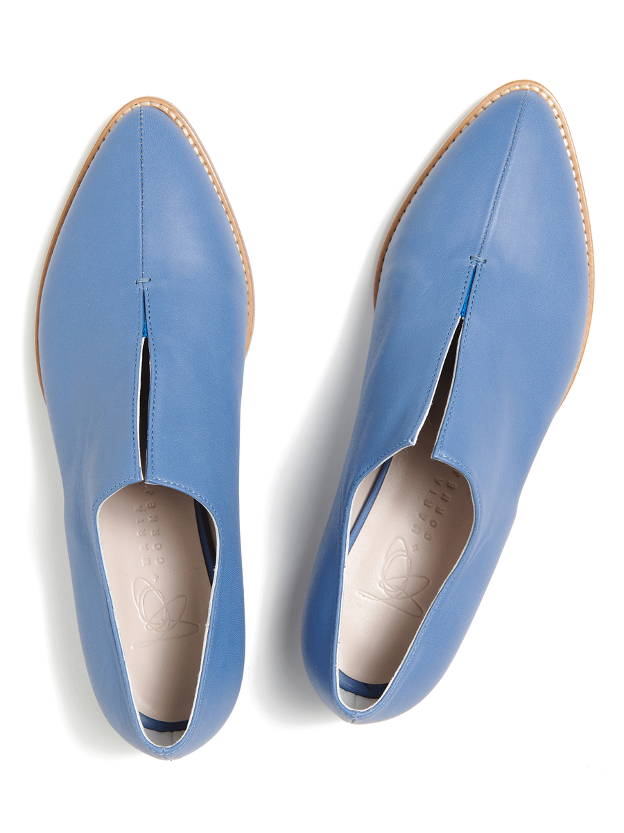 The Kiara Oxford by Zero + Maria Cornejo is a pair of stylish blue leather slip-on shoes featuring pointed toes, tan soles, and wooden heels. Photographed from above on a white background, their Italian sizing ensures a perfect fit and adds an elegant touch.