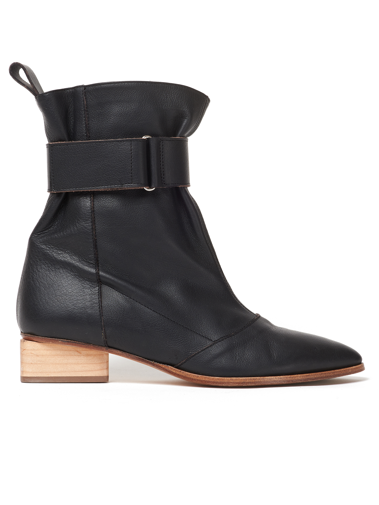 The Adina Boot by Zero + Maria Cornejo is a black Nappa leather ankle boot featuring a wooden low-block heel, a rounded toe, and a wide strap around the ankle secured by an adjustable Velcro strap. It also includes a pull tab at the back for ease of wearing.